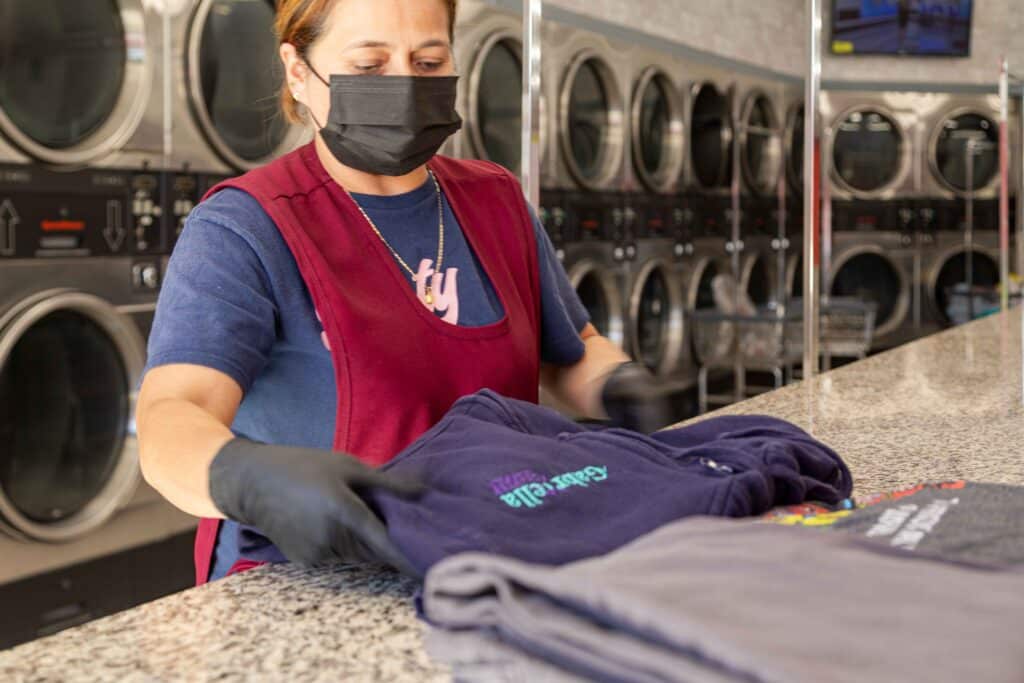 Woman folding clothes while wearing a face mask and gloves at 24/7 laundry near USC